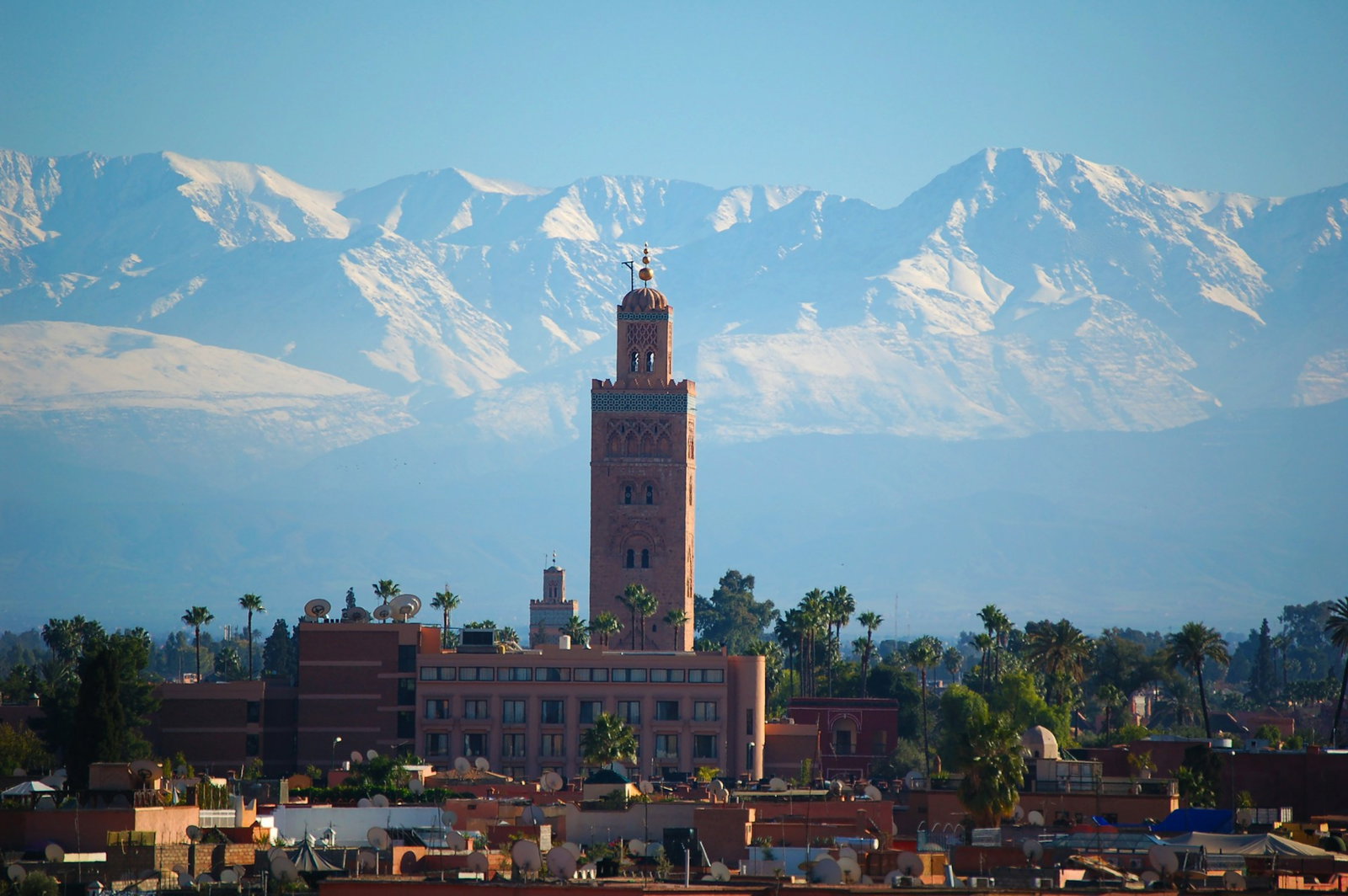 Cityscape with brown tower and backdrop of snow-capped mountains and blue sky