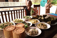A lady sitting at a table full of traditional Laotian food