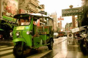 A green Tuk Tuk driving down a busy street in Chinatown in Bangkok