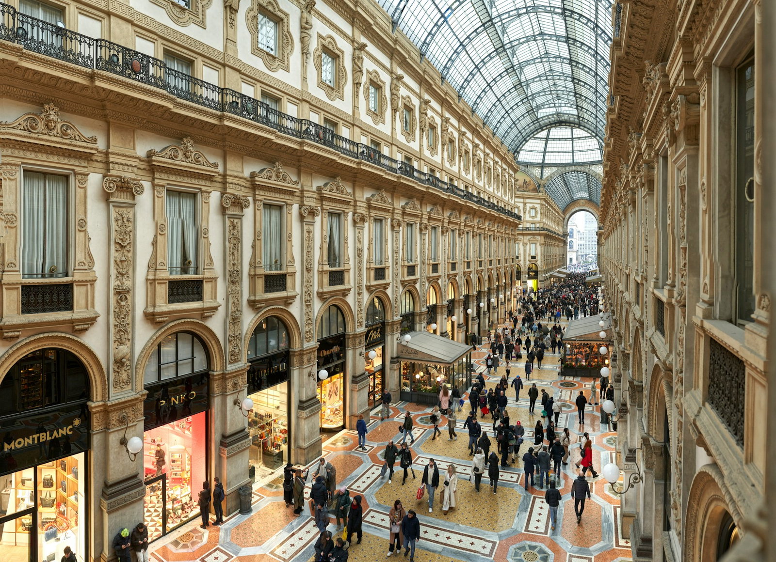 High up shot of luxurious mall with classic beige and cream architecture and lots of people near the black shopfronts