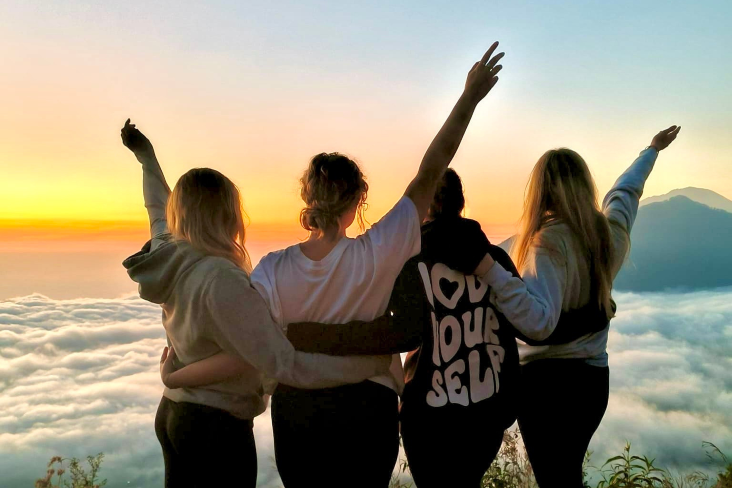 Travellers with arms in the air whilst watching the sunrise at Mount Batur in Bali