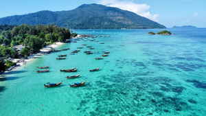 Boats sitting in pristine blue water on a beach with islands in the background