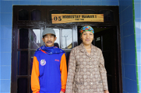 Two people standing in front of a building with a sign reading 'Homestay Mawari'