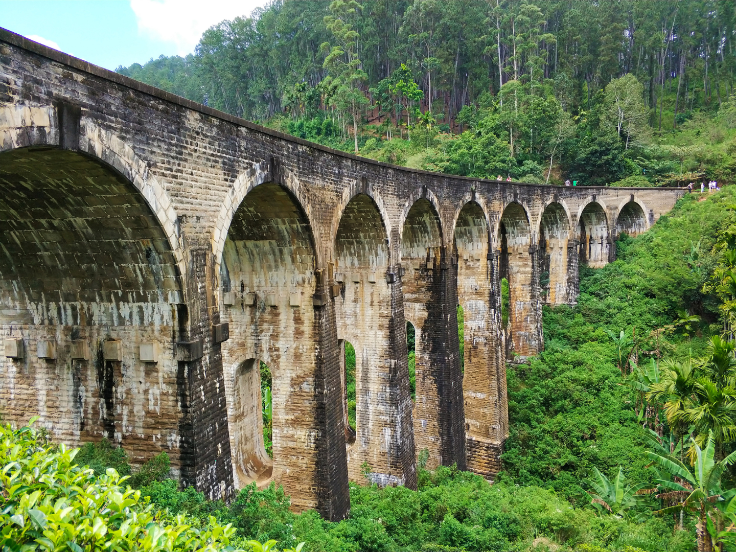 Traditional brick bridge with nine arches surrounded by green shrubbery and forested hills