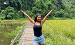 Woman solo travelling Vietnam on a group trip, standing in a rice field with arms in the air