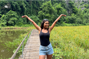 Woman solo travelling Vietnam on a group trip, standing in a rice field with arms in the air