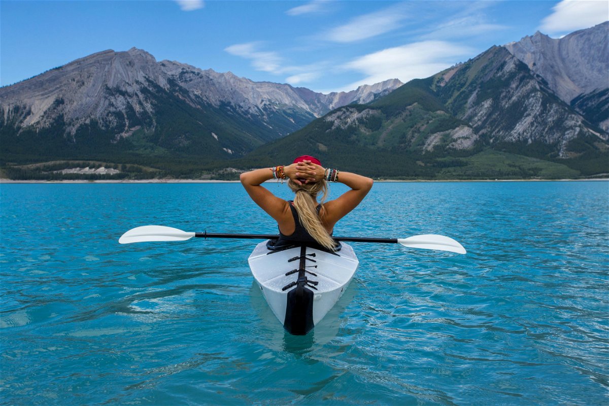 Girl on single kayak boat staring off into mountains on a lake.