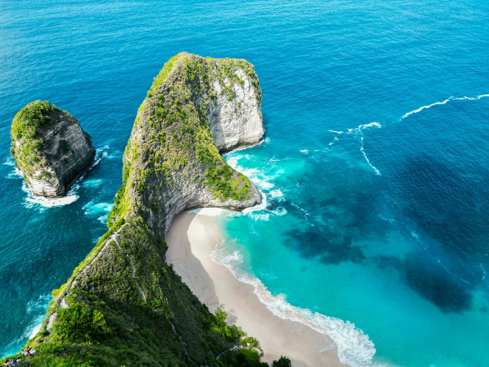 Tall grey cliffs covered in emerald flora by secluded white sandy beach and surrounded by bright sapphire ocean, Nusa Penida