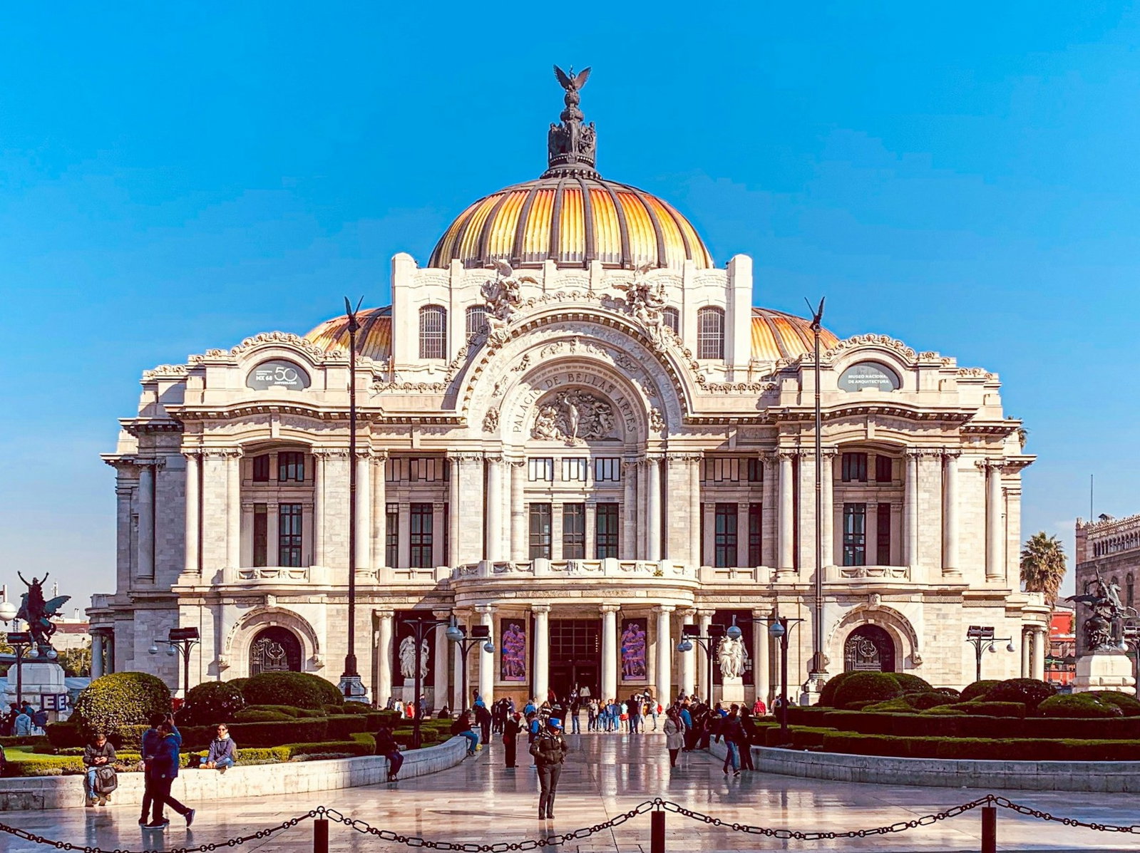 Art Nouveau building with columns built from white stone with curved orange and grey rooftop, with people outside