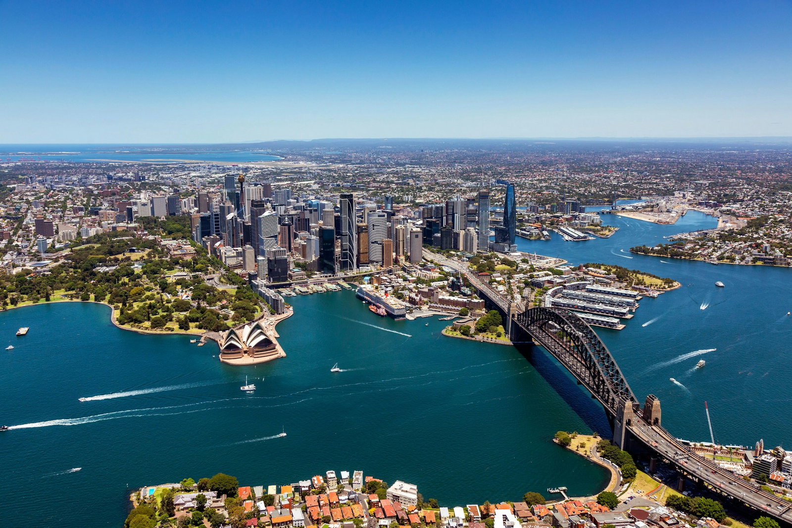 Aerial shot of city with ocean and bridge connecting, bright blue sky, Sydney