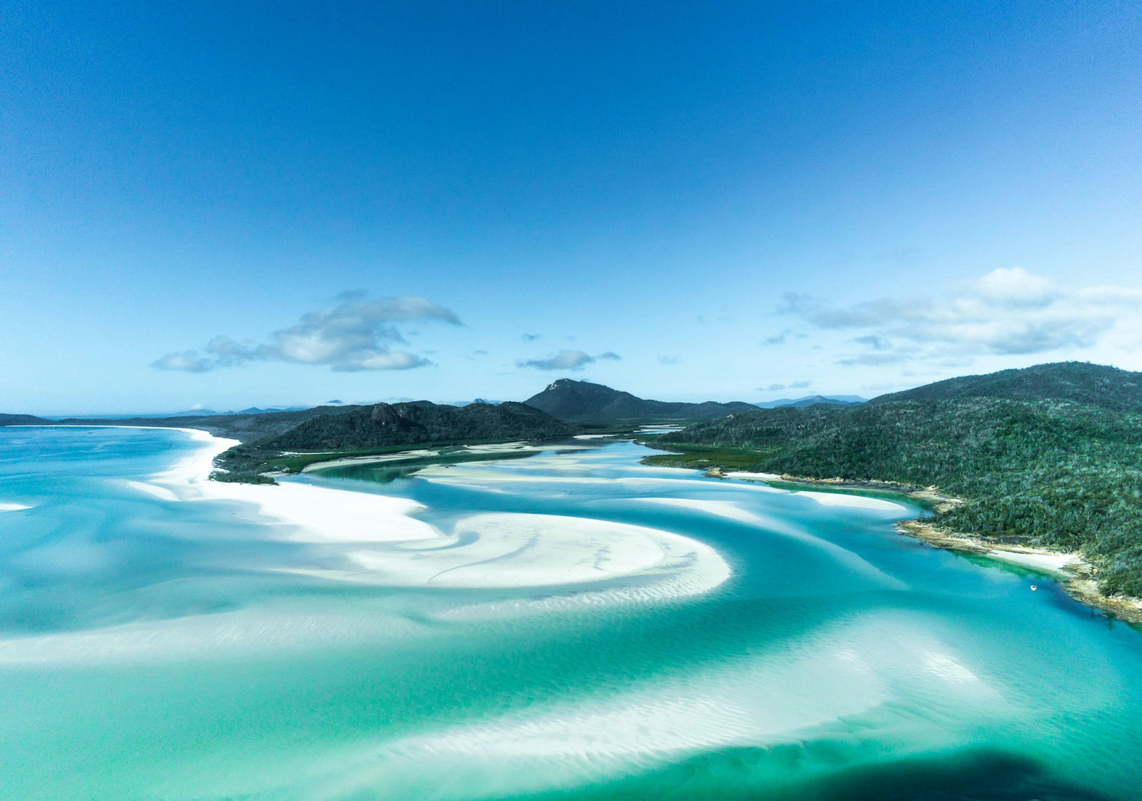 Swirling white sands and turquoise ocean with lush tropical island in background, The Whitsundays