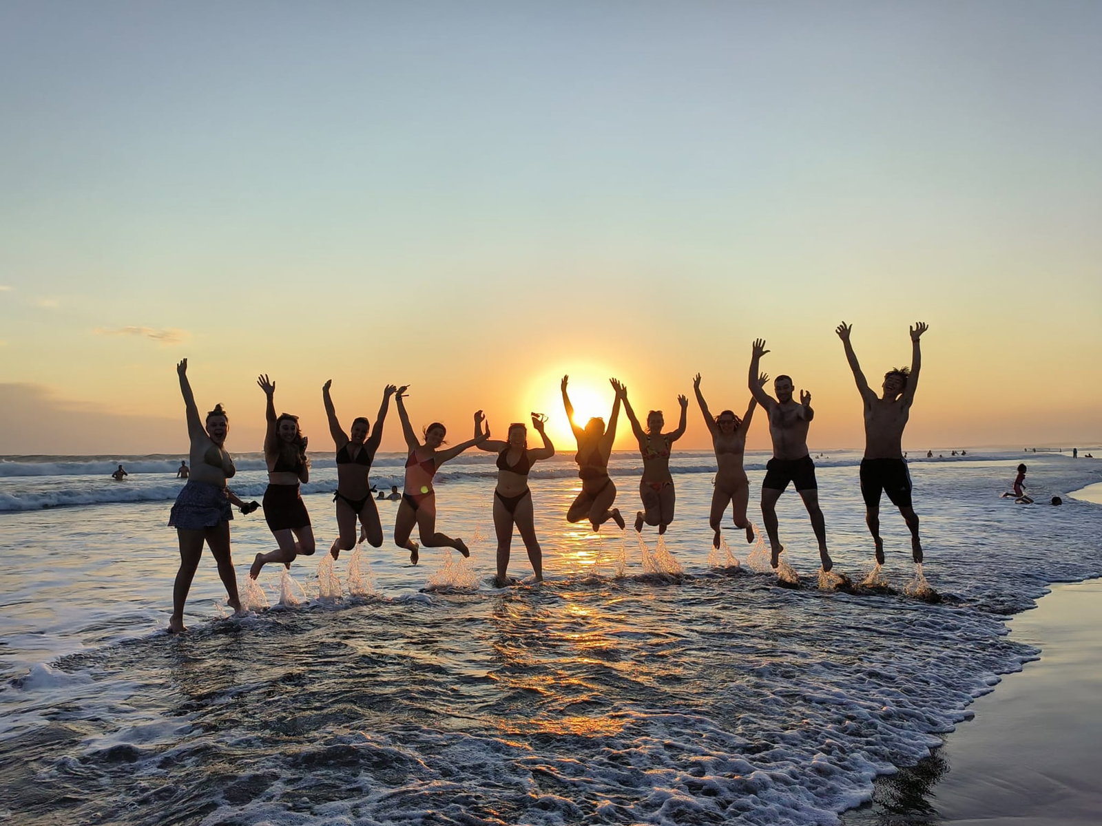 Travellers jumping on balinese beach with sunset behind them