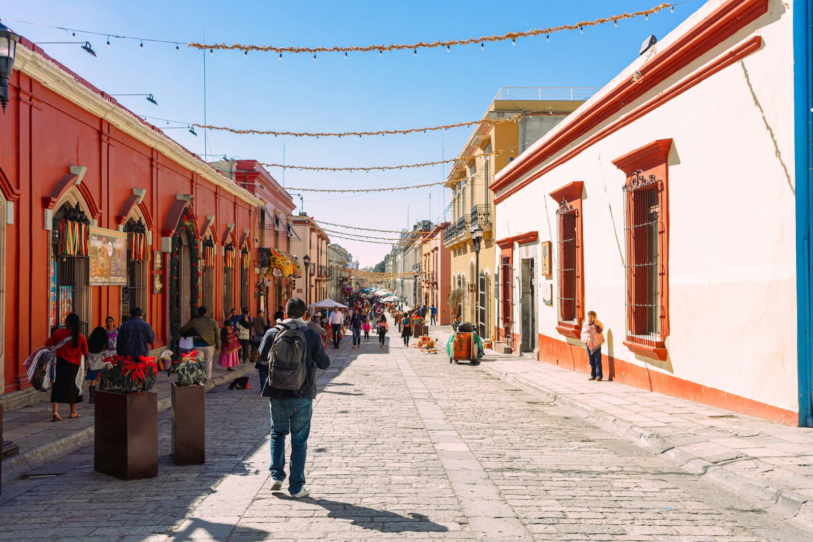Colourful red and white traditional buildings on cobblestone streets with people walking underneath decorations from ceiling