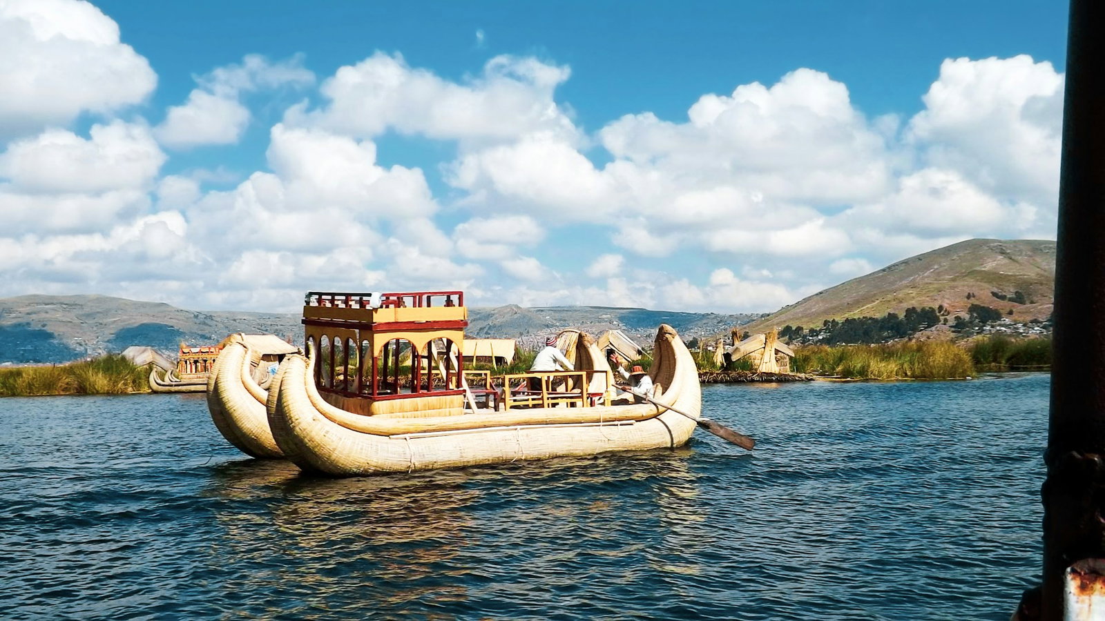 Traditional Peruvian boat sailing across Lake Titicaca's indigo blue lake surrounded by valleys on a cloudy day