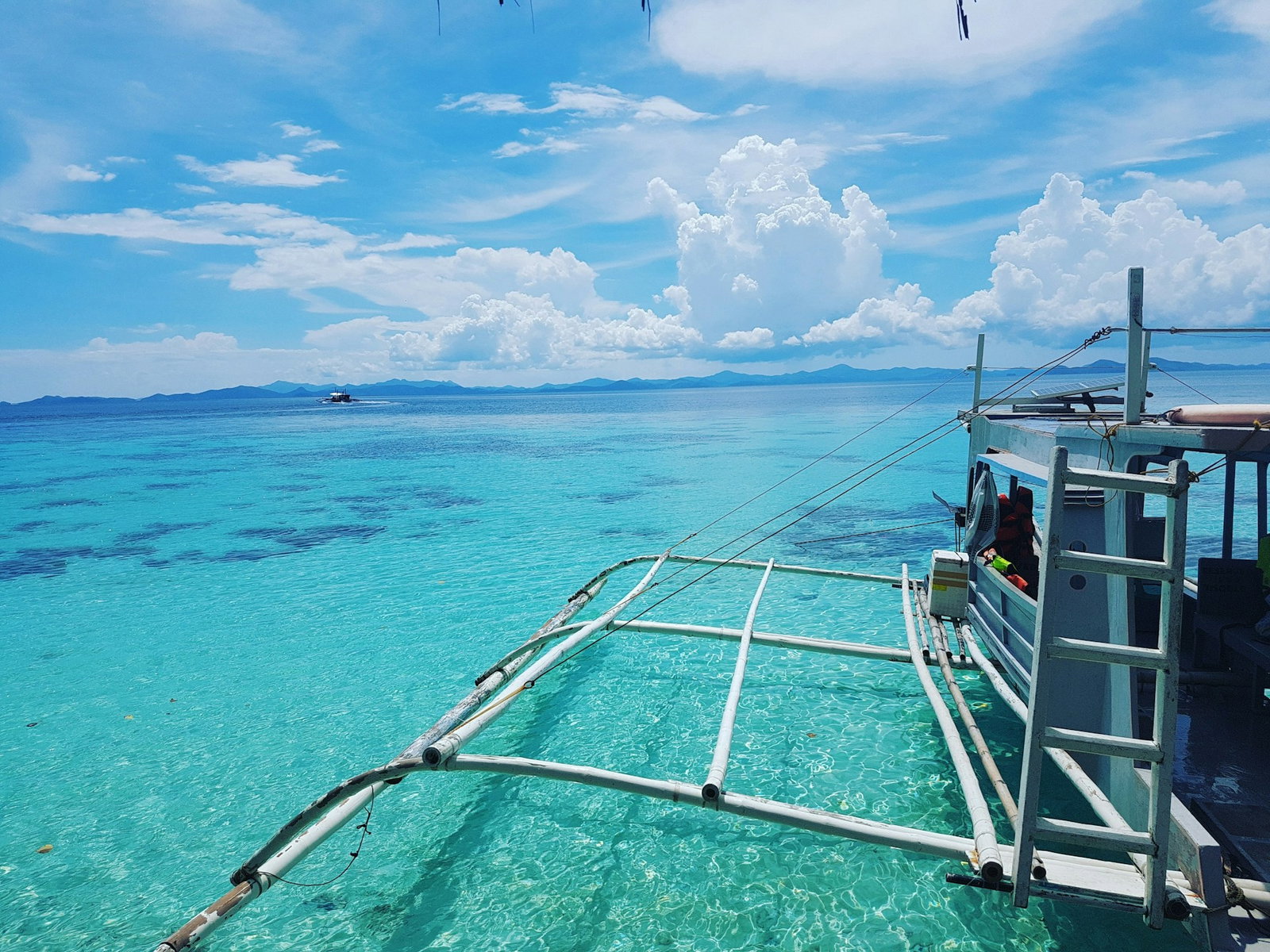 Traditional Filipino boat sailing through bright turquoise waters with a cloudy blue sky in the distance