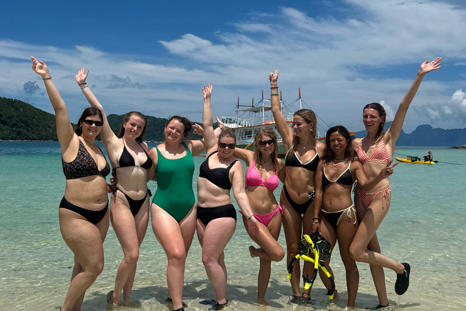 Group of travellers on the beach in the Philippines with their arms in the air