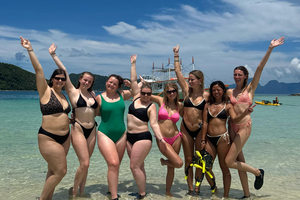 Group of travellers on the beach in the Philippines with their arms in the air