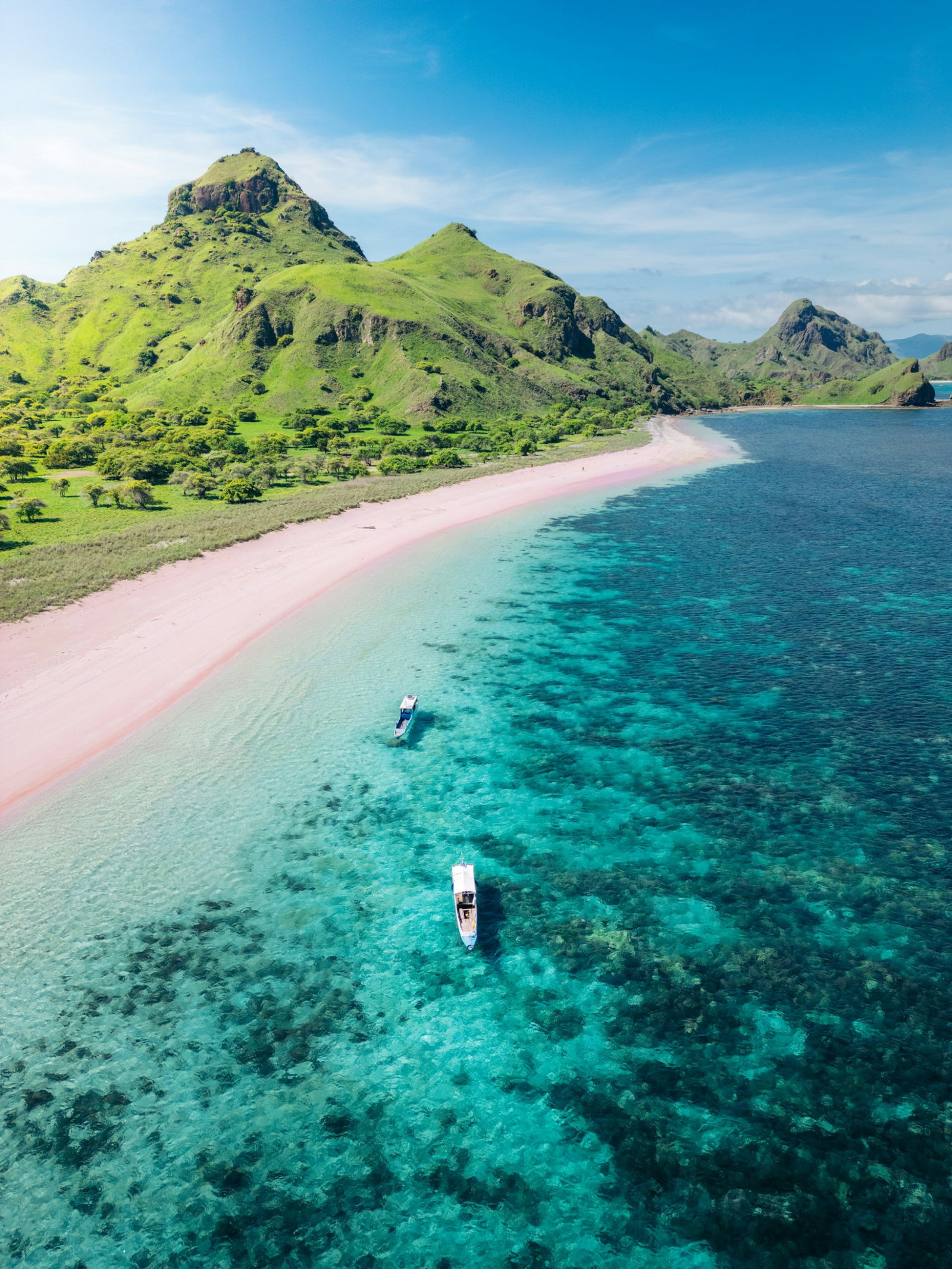 Pink beach with emerald volcano mountains and bright turquoise ocean with two little boats in the ocean