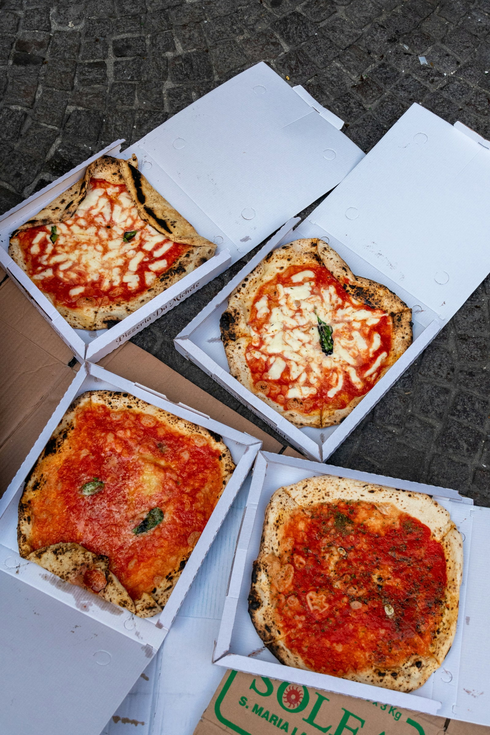 Four white boxes containing Neopolitan style pizza, two with cheese and two without