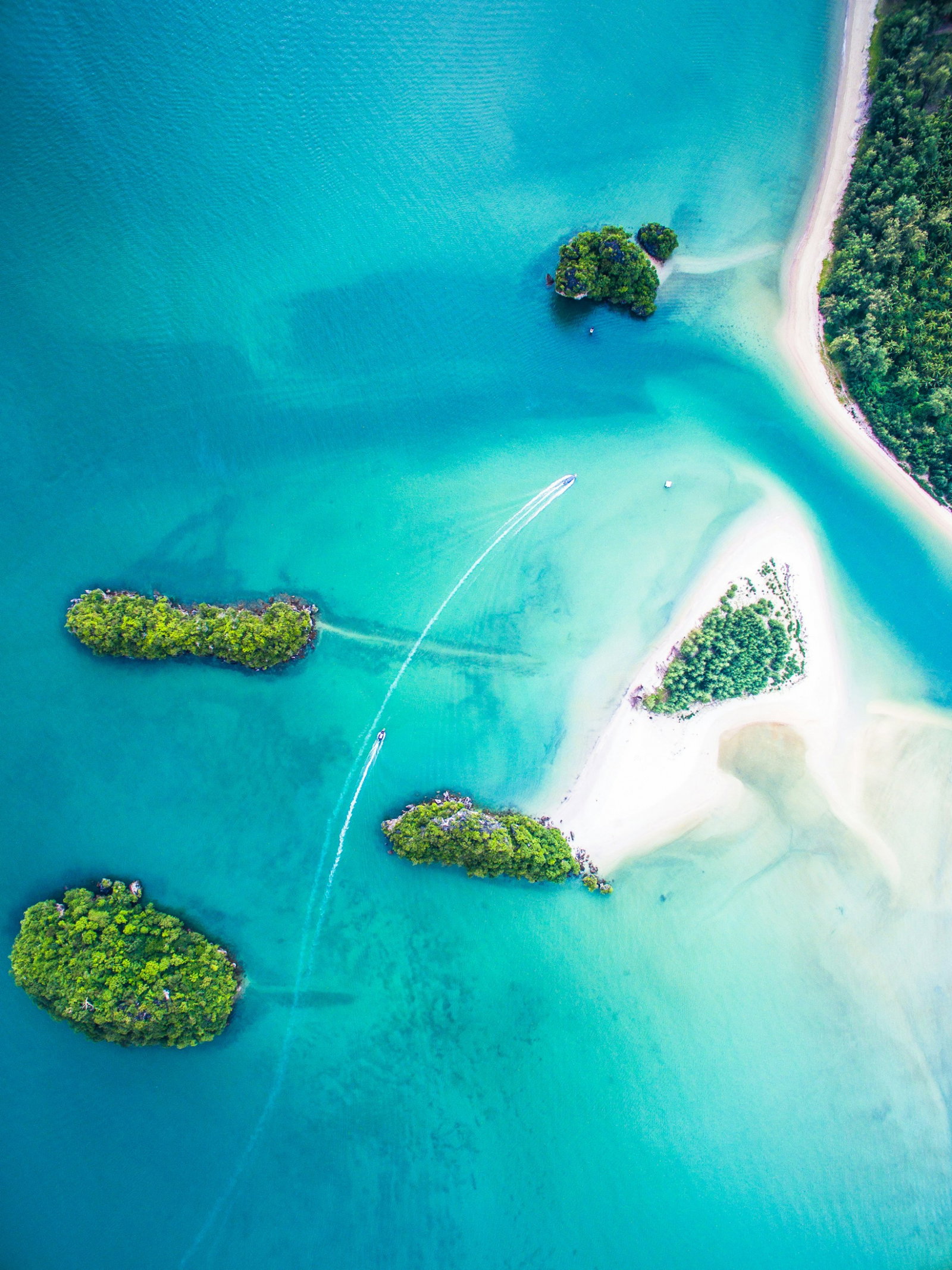 Aerial shot of bright turquoise waters and white sands with boats gliding in water, little islands covered in lush vegetation