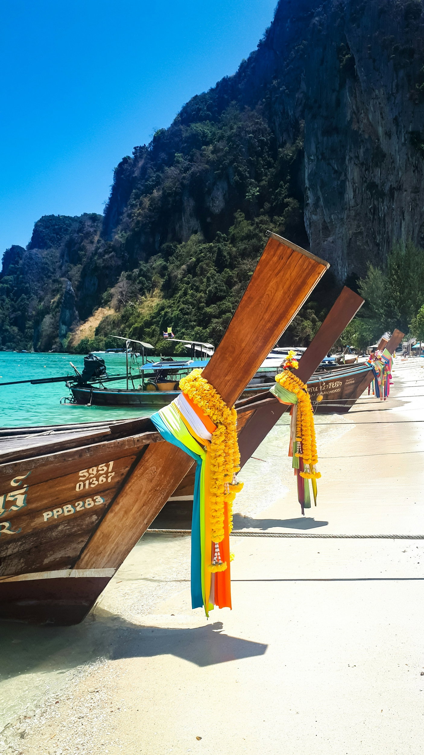 Traditional wooden boats with colourful ties on golden beach with tall jungle-clad cliff in background with clear blue sky