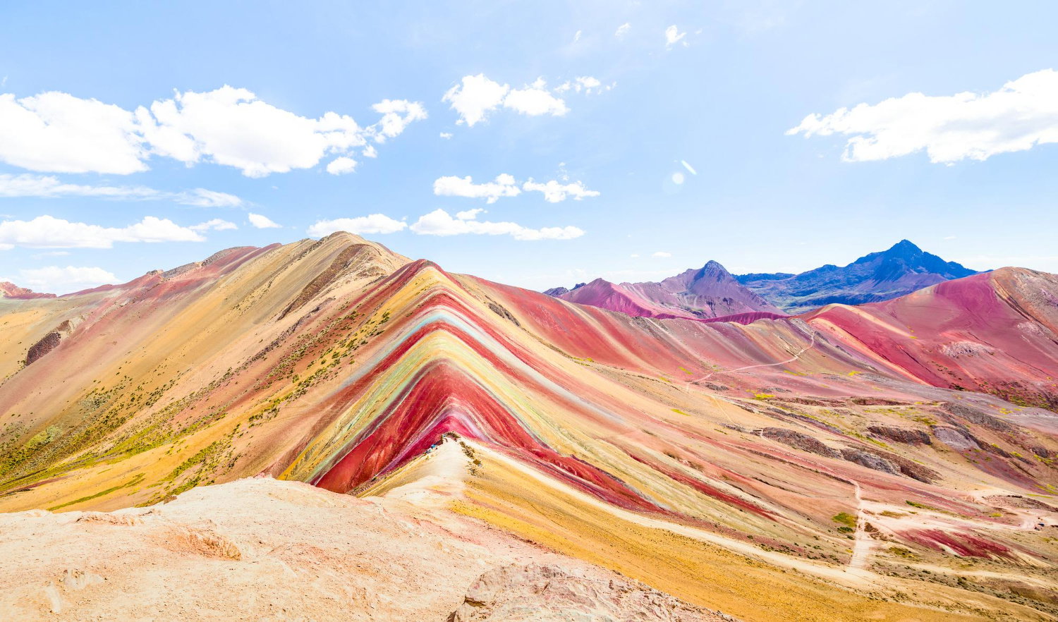Candy coloured striped rainbow mountains on a sunny day with some white clouds