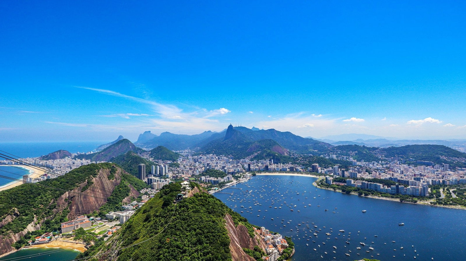 Cityscape of Rio de Janeiro with lush green hills, golden beaches and modern skyscrapers curving around the sea on clear day