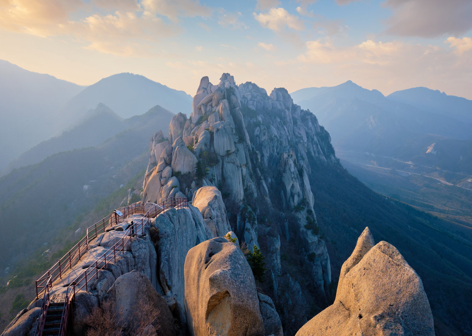 Smooth rocks atop of a mountain with stairs leading up, surrounded by green mountains at dawn