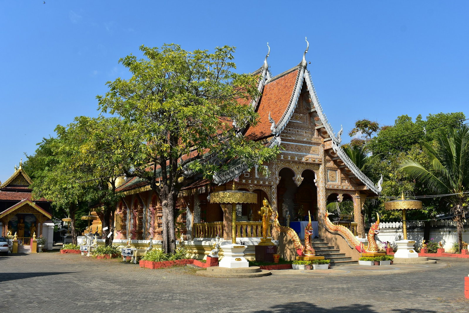 Small and traditional Thai temple with ornate details and mini statues, surrounded by trees
