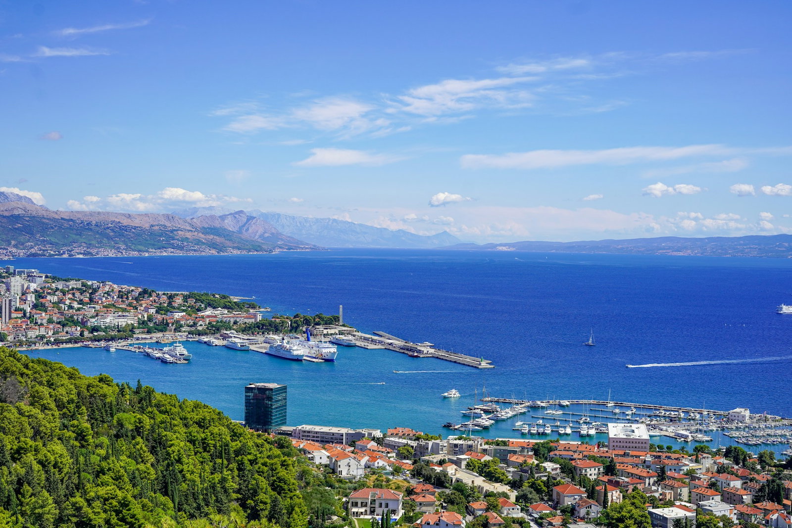 Lush viewpoint of emerald hills and Croatian city with modern and traditional architecture, port and blue ocean