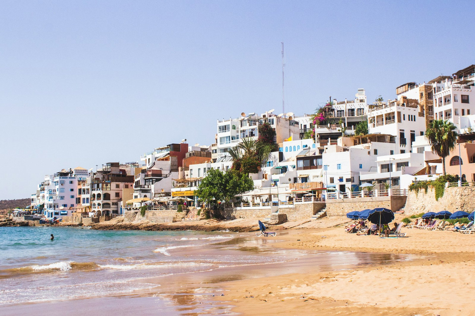 White-washed buildings by golden beach with crashing waves and sunbeds