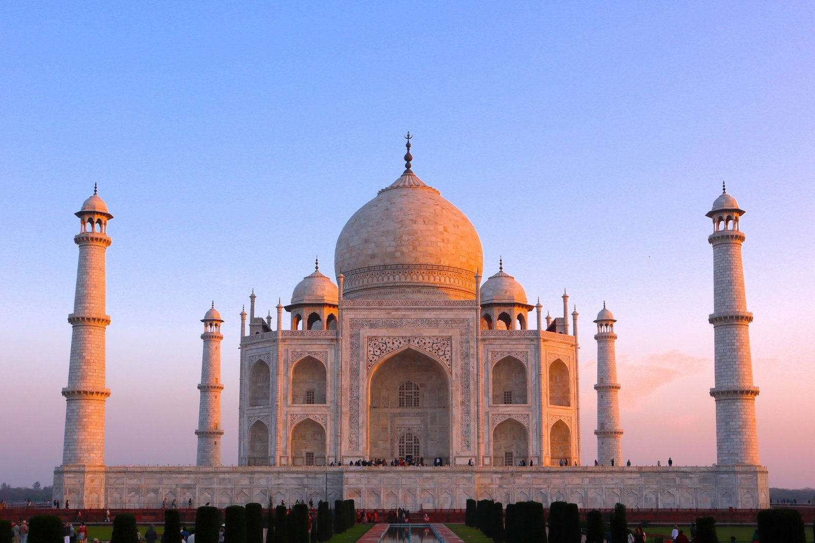 Stunning white palace with bell-shaped rooftops and towers on a raised platform overlooking row of bushes and fountain