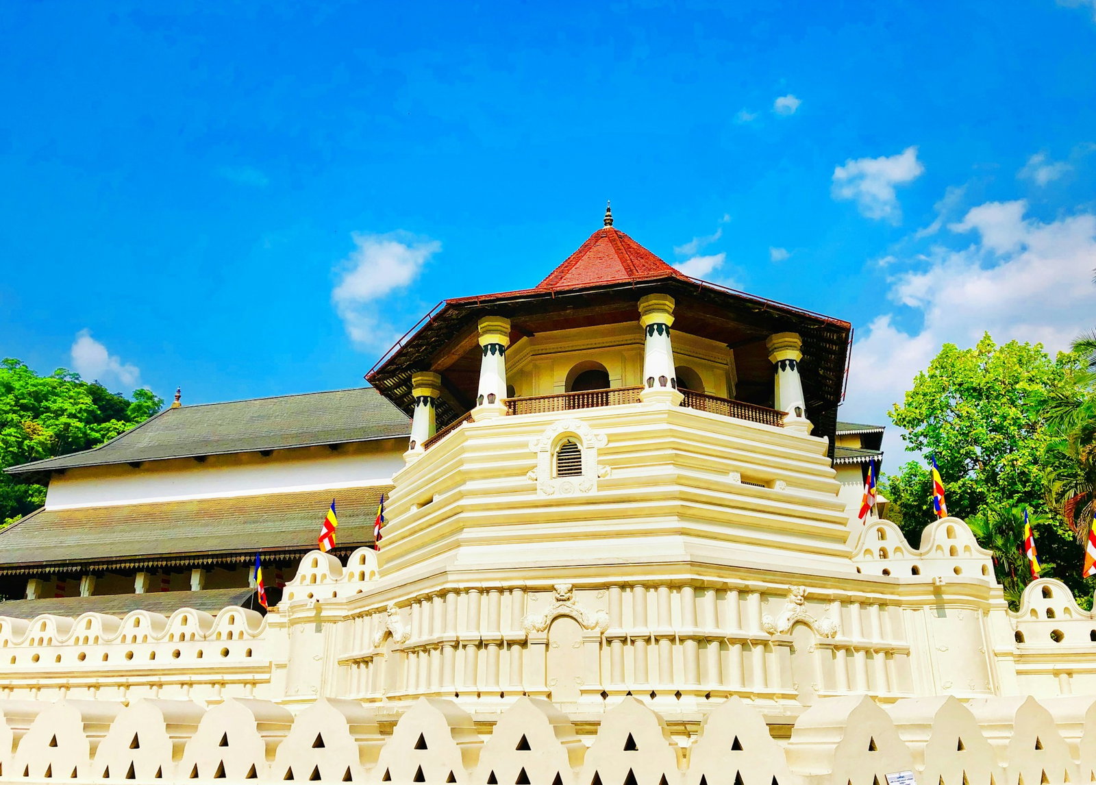 Sacred temple with pale yellow architecture and a red and grey-green rooftop on a blue sky day with some clouds