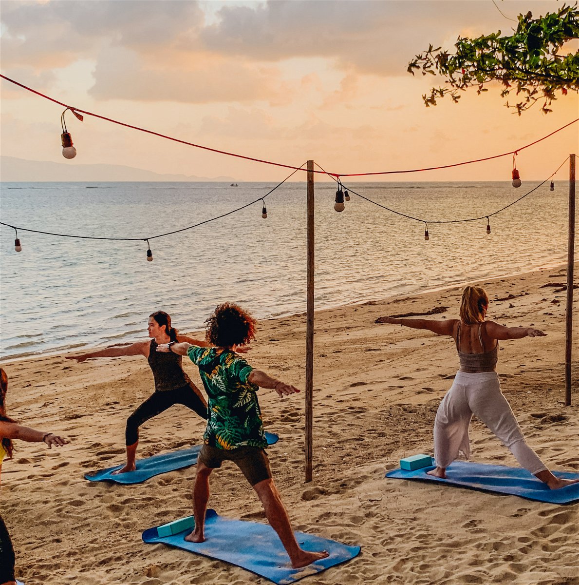 Yoga on the beach at sunset with lights handing above