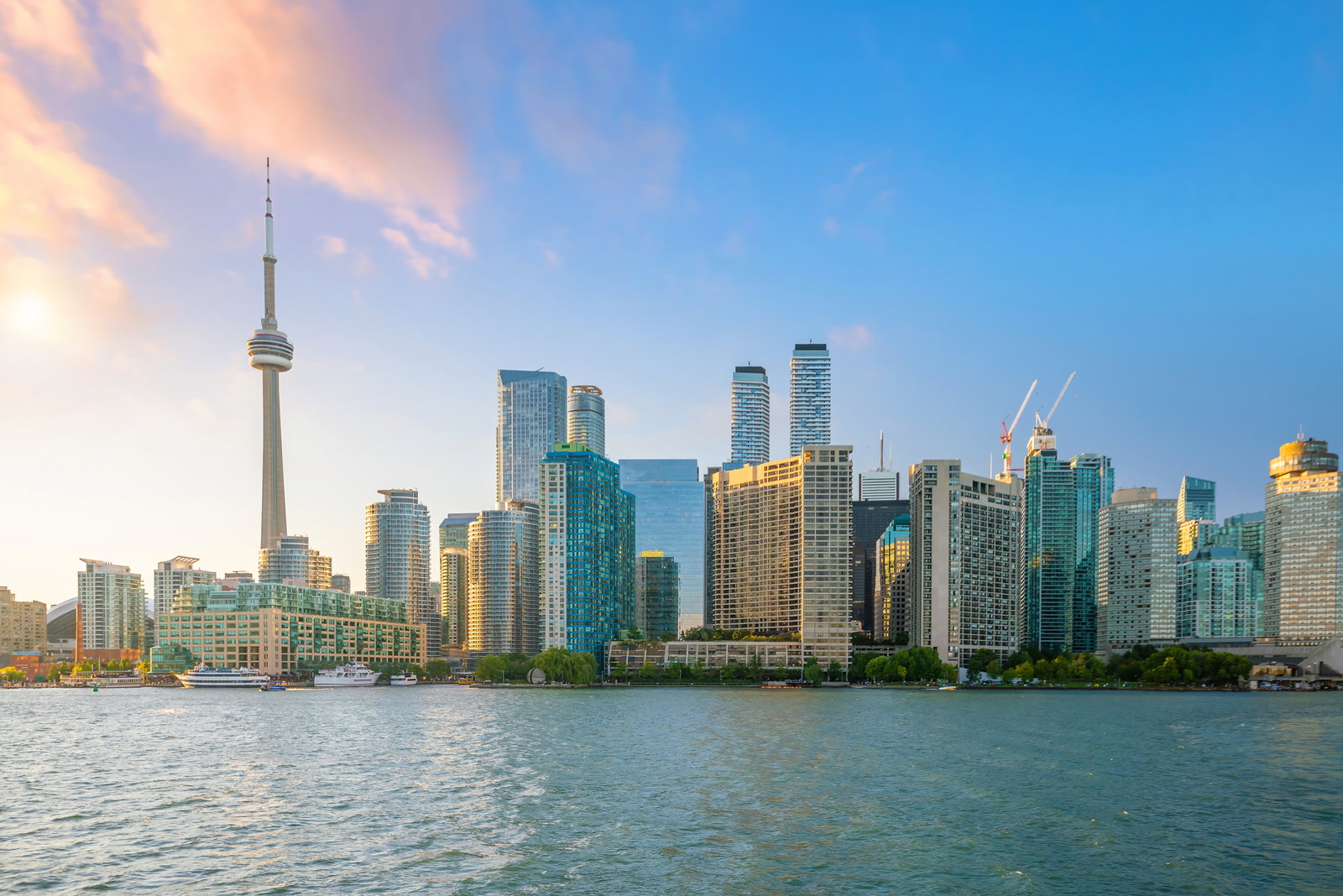 City skyline from lake with lots of modern skyscrapers and some green shrubbery with light sunset haze in blue sky