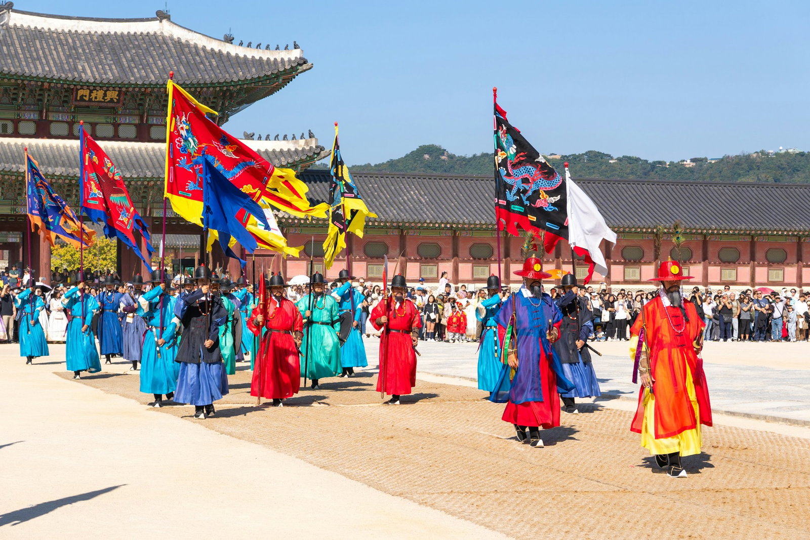 People dressed in colourful hanbok and waving traditional flags outside palace with crowd watching the ceremony