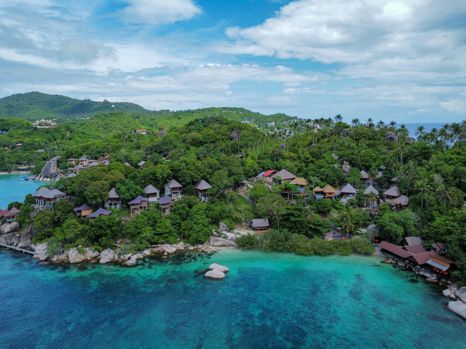 Tropical island with traditional stilt houses woven into jungle, rocky sea bed and turquoise ocean, cloudy day