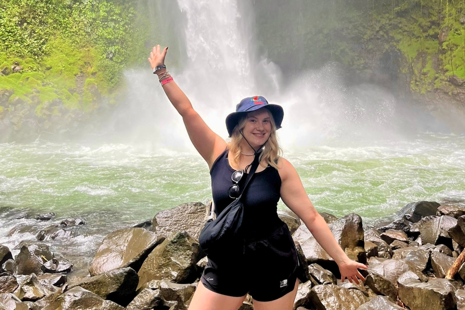 Traveller with arms in the air on a Costa Rica tour in front of La Fortuna Waterfall, surrounded by green jungle