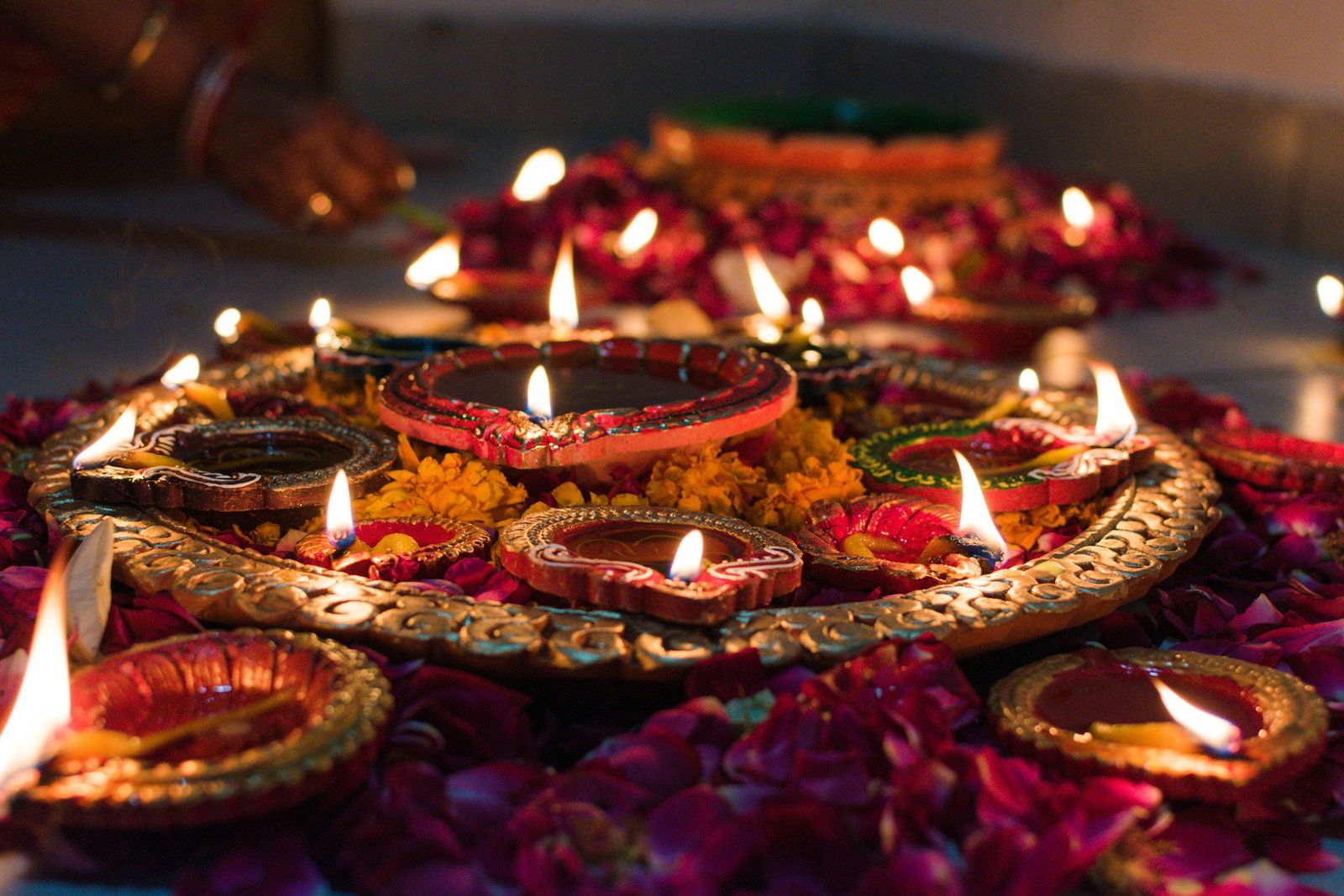 Red mosaic candle plates lit for Diwali, laid on bed of flowers on the floor