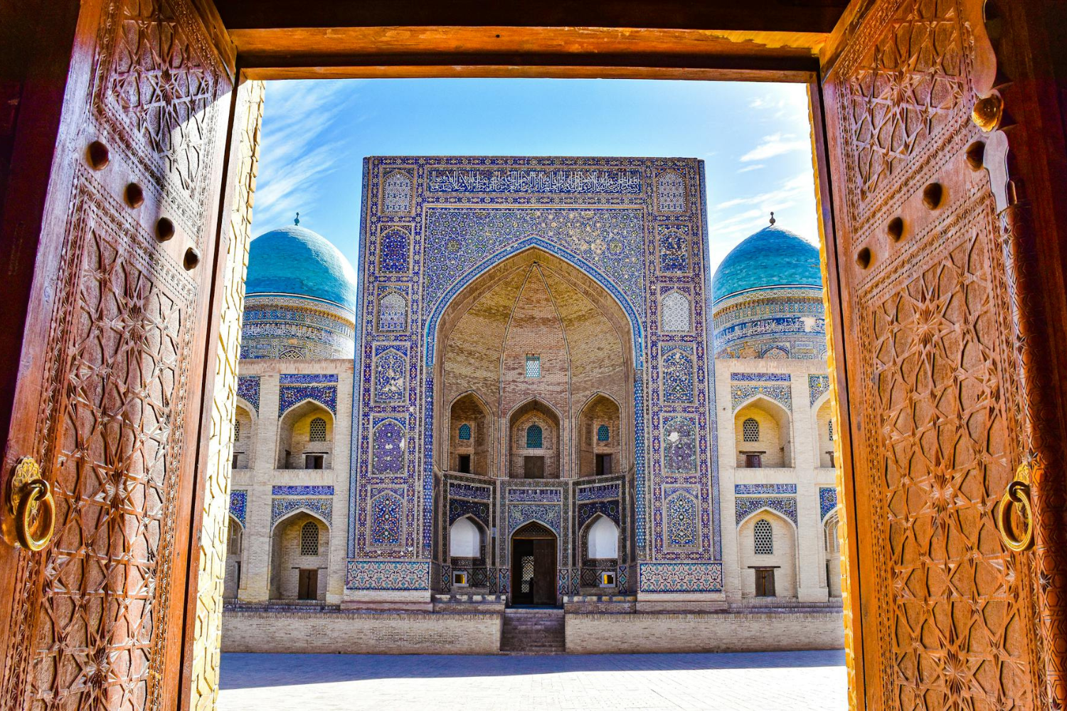 Brown doors leading onto traditional mosaic building with turquoise domes in Uzbekistan