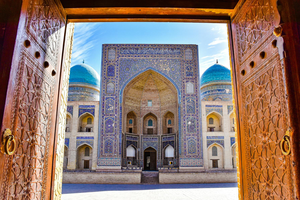 Brown doors leading onto traditional mosaic building with turquoise domes in Uzbekistan