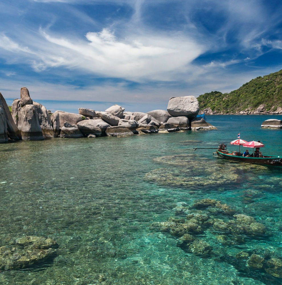 A boat sits on pristine, clear water on the edge of Koh Tao island