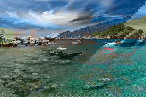 A boat sits on pristine, clear water on the edge of Koh Tao island
