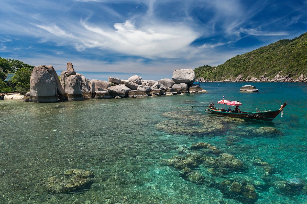 A boat sits on pristine, clear water on the edge of Koh Tao island