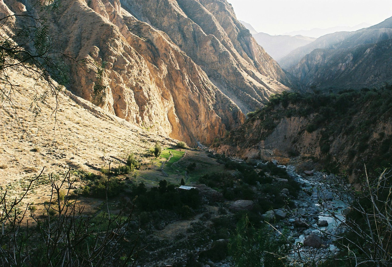 Valley with rugged brown mountains curving in at both sides, a little river stream in the centre, Colca Canyon