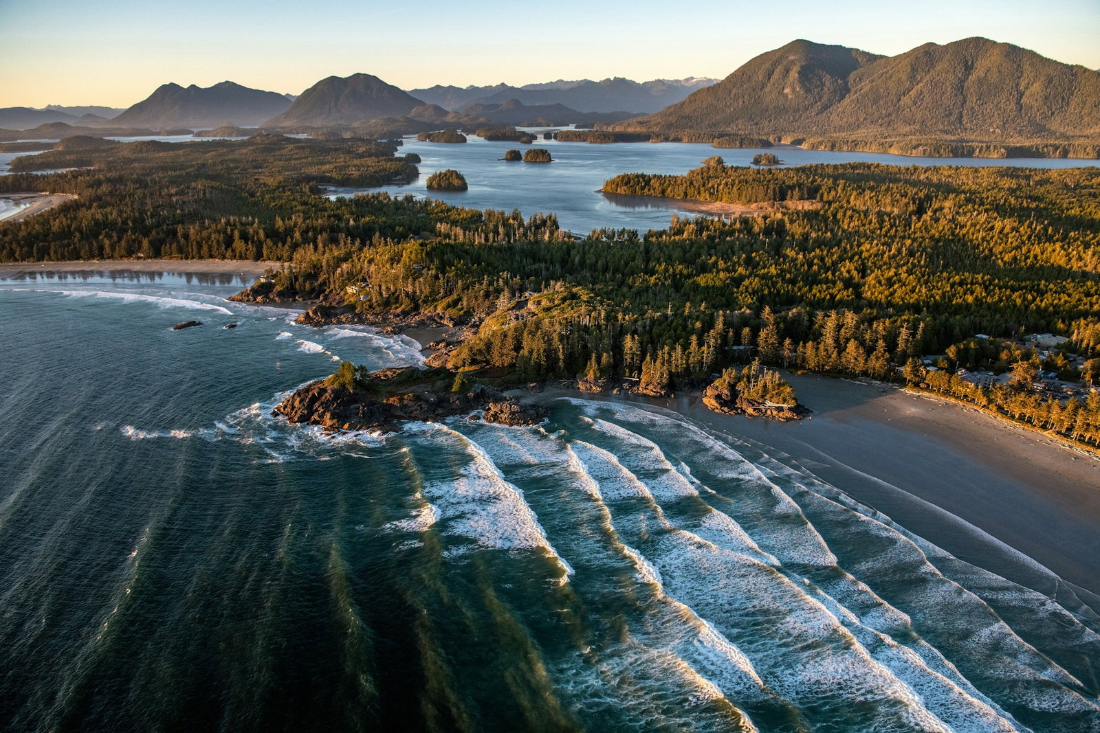 Ancient forest stretches by the coast with grey beaches and dark ocean waves with little islets in the distance
