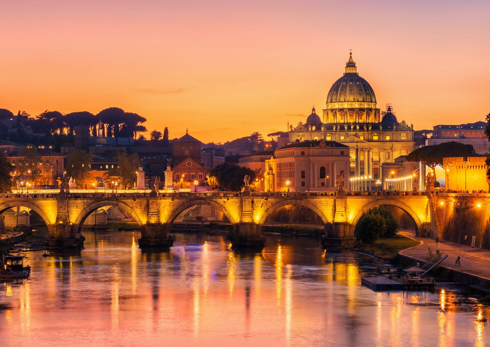 river at sunset with classic stone bridge and stunning chapel illuminated by lanterns, some shadowed trees in the distance