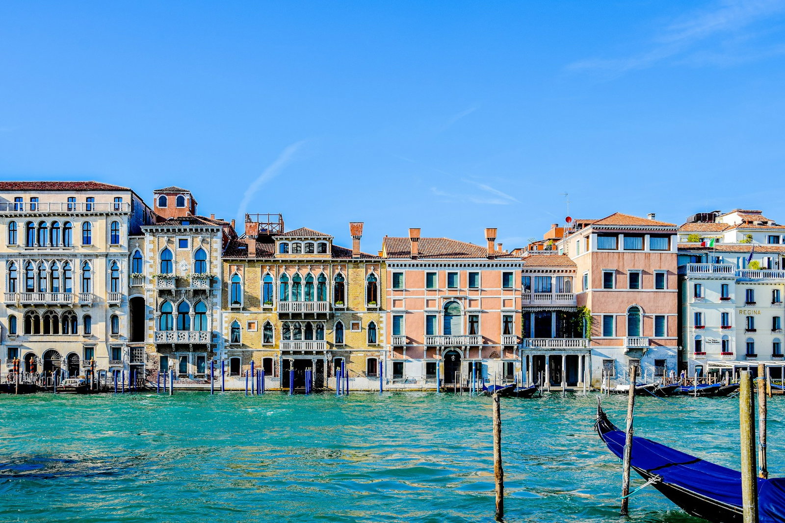 Bright sapphire waters facing out to pastel coloured buildings with blue boats docked in the water under clear blue skies