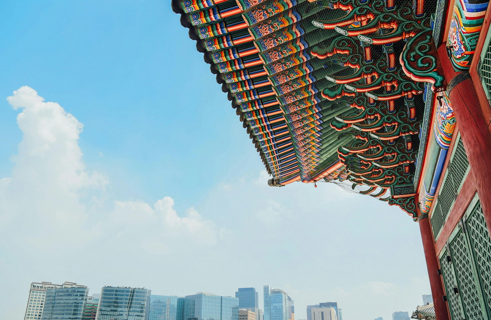 Colourful roof of a palace with modern cityscape in the centre under blue skies with mist of clouds