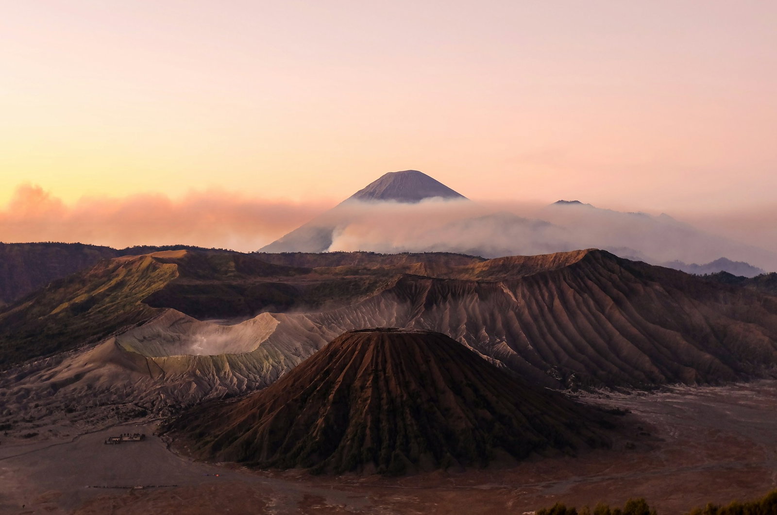 Crater volcanoes and more volcanoes in the distance with a veil of mist under baby pink skies at sunrise